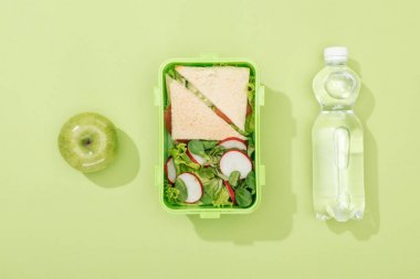 top view of lunch box with salad and sandwiches near bottle with water and green apple clipart
