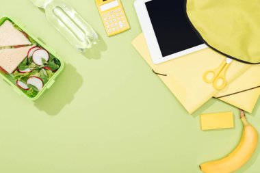 öğle yemeği kutusu, kırtasiye ve su şişesi yakınında dijital tablet ile sırt çantası üst görünümü