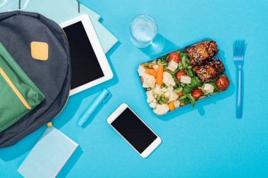 öğle yemeği kutusu, akıllı telefon, kırtasiye, akıllı telefon ve su bardağı yakınında dijital tablet ile sırt çantası üst görünümü