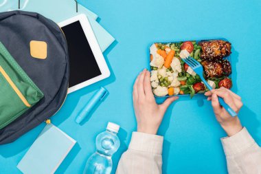 klasörler, kırtasiye, su şişesi ve dijital tablet ile sırt çantası yakınında öğle yemeği kutusu tutan kadın kırpılmış görünümü