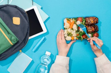 cropped view of woman holding lunch box near backpack with folders, stationery, bottle of water and digital tablet clipart