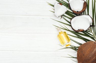 beyaz ahşap yüzeyüzerinde yeşil palmiye yaprağı üzerinde şişe hindistan cevizi yağı üst görünümü