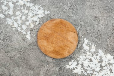 top view of coconut shavings near wooden board on grey textured background clipart