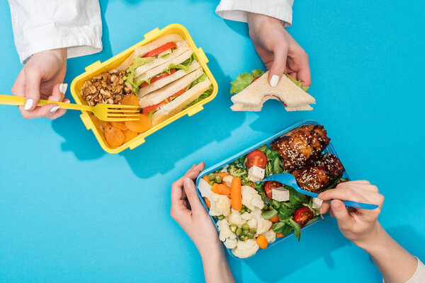 cropped view of two women holding forks over lunch boxes with food