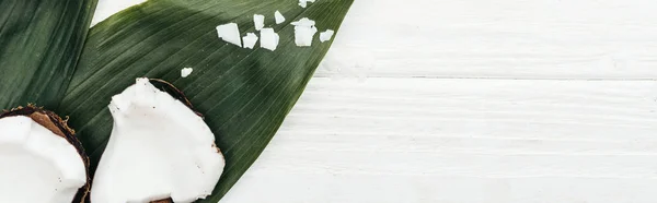 top view of coconut pieces on palm leaves on white wooden surface with copy space, panoramic shot