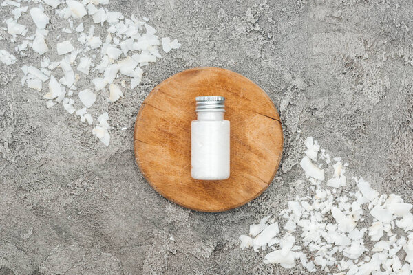top view of coconut shavings near wooden board with coconut cream on grey textured background