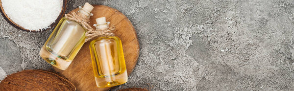 top view of coconut oil in bottles on wooden board on grey textured background with copy space, panoramic shot