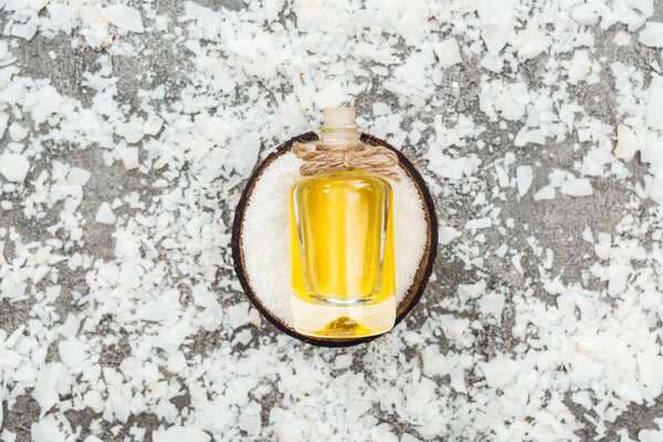 top view of oil in bottle on coconut half on grey background with coconut shavings