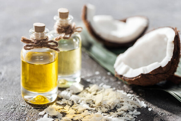 selective focus of bottles with coconut oil near coconut halves and shavings on grey background