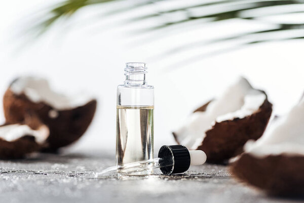 selective focus of open bottle with coconut serum near dropper and cracked coconuts