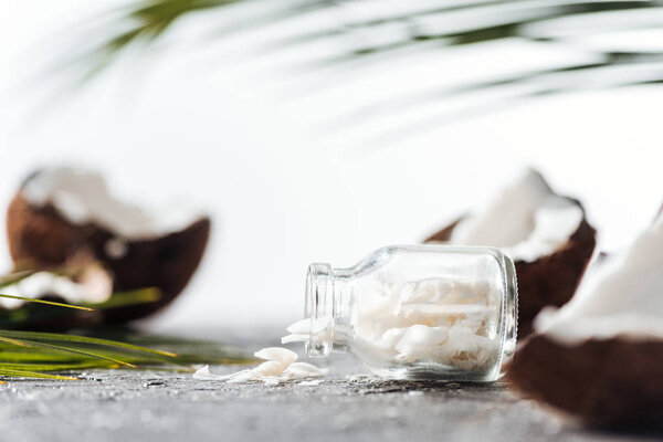 selective focus of glass bottle with coconut shavings near cracked coconuts and palm leaves