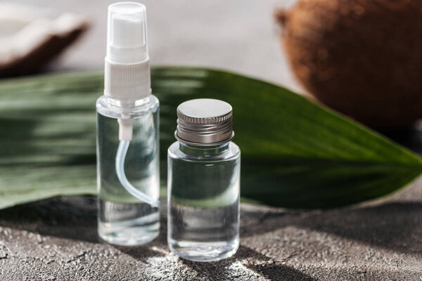selective focus of bottles with coconut water near palm leaf on grey textured background