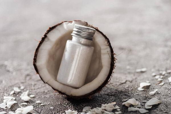 bottle with white coconut cream in coconut half on grey textured background