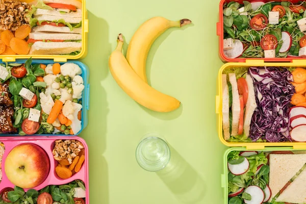 Top view of lunch boxes with food near glass of water and bananas — Stock Image Top View Lunch Boxes Food Glass Water Bananas Stock Picture