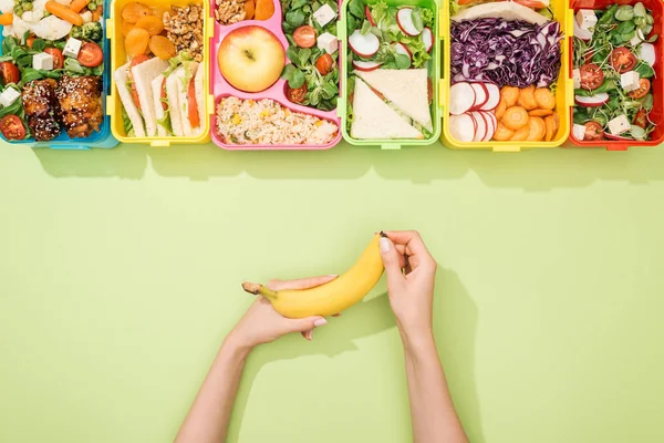 Cropped view of woman holding banana in hands near lunch boxes with food — Stock Image Cropped View Woman Holding Banana Hands Lunch Boxes Food Stock Picture