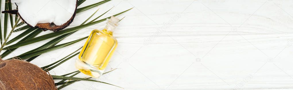 top view of coconut oil in bottle on green palm leaf on white wooden surface, panoramic shot
