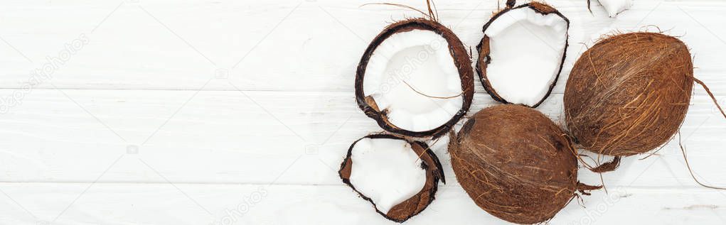top view of cracked and whole coconuts on white wooden surface, panoramic shot