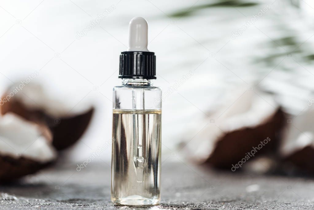 selective focus of bottle with coconut serum and dropper near cracked coconuts