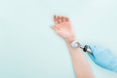 mavi izole dermatoskop ile kadının elini inceleyen doktor kırpılmış görünümü