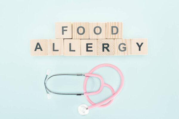 top view of wooden blocks with food allergy lettering near stethoscope isolated on blue 