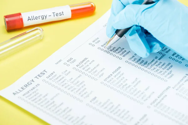 黄色で分離されたアレルギー試験レタリングを持つ試験管の近くのアレルギー試験フォームでラテックス手袋充填中の女性のトリミングビュー — ストック写真