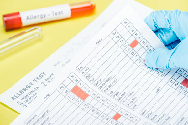 cropped view of woman holding allergy test results near test tubes with allergy test lettering isolated on yellow