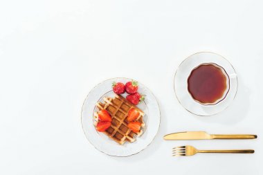 beyaz üzerinde çay, çatal ve bıçak ile fincan yakın tabakta çilek ile waffle üst görünümü