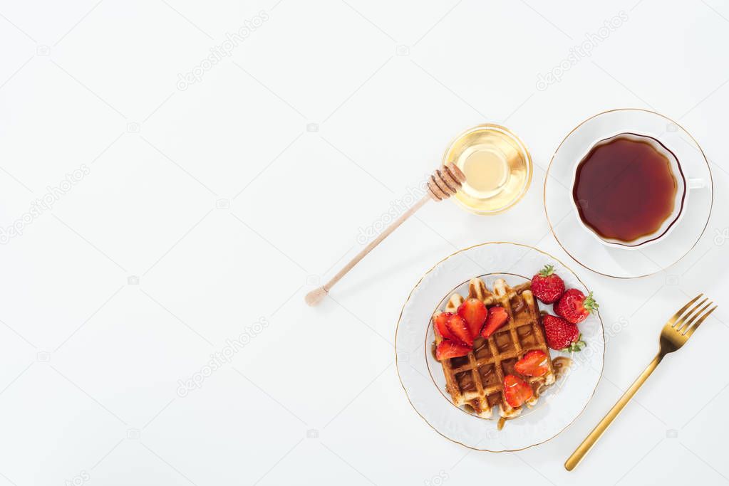top view of delicious breakfast with waffle, strawberries and tea on white