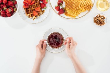 beyaz çilek ve waffle ile tabak yakınında çay kaşığı ve çay bardağı tutan kadın kırpılmış görünümü