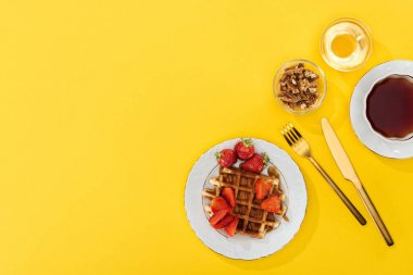 sarı üzerinde çatal yakın waffle ve çilek, fındık, bal ve çay üst görünümü