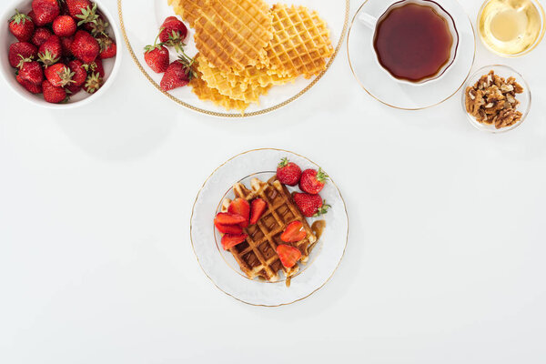 top view of delicious breakfast with waffles, strawberries and tea on white