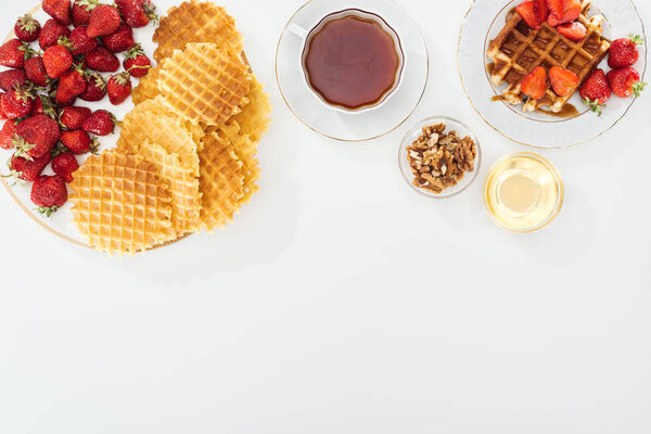 top view of waffles, strawberries, honey, nuts and tea on white