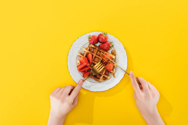 cropped view of woman cutting waffle on plate on yellow