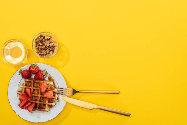 top view of waffles, berries, honey and nuts near cutlery on yellow