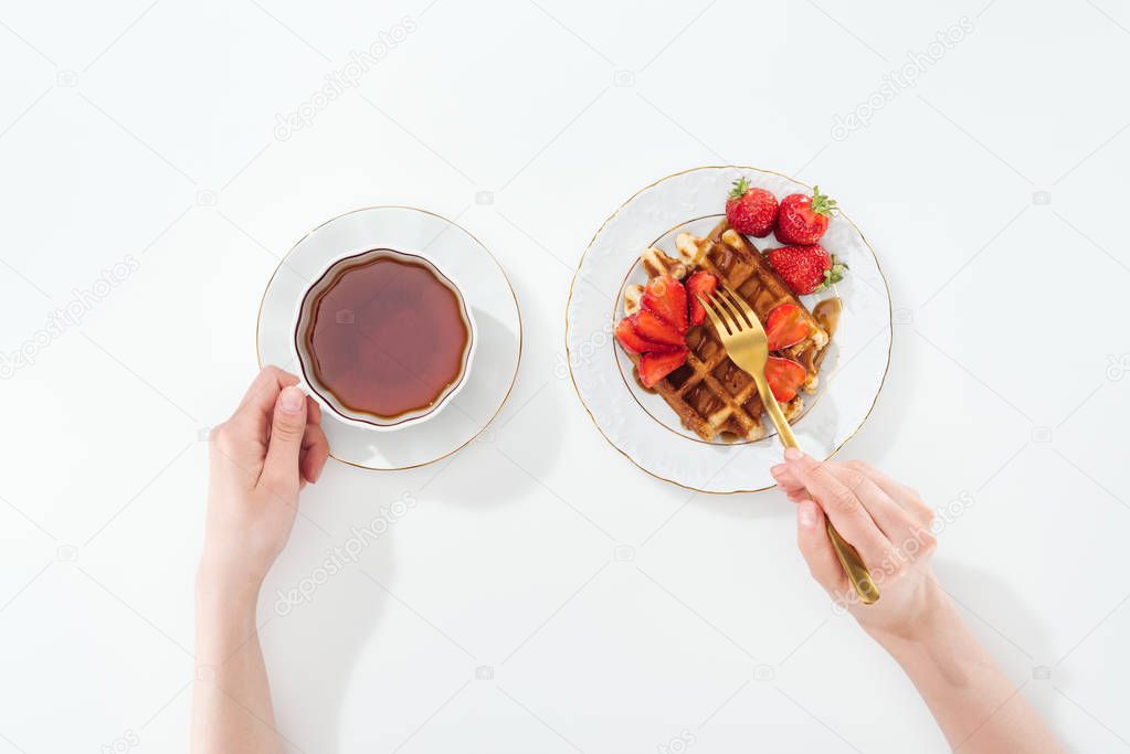 cropped view of woman holding cup with tea and fork on white