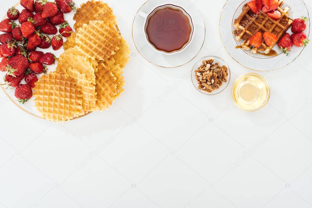 top view of waffles, strawberries, honey, nuts and tea on white