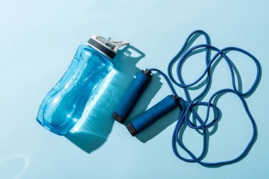 top view of sport bottle with water near skipping rope on blue  clipart
