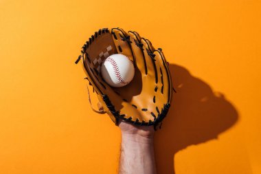 cropped view of man holding softball in brown baseball glove on yellow  clipart