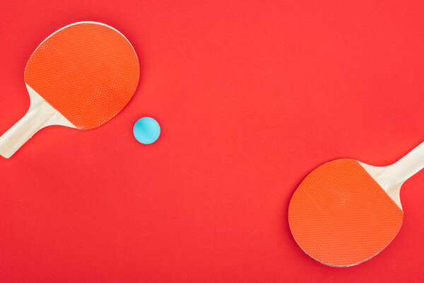 top view of blue ping pong ball near rackets isolated on red 