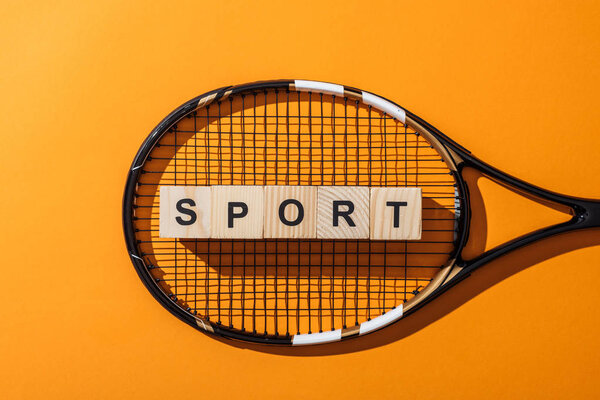top view of wooden cubes with sport lettering near tennis racket on yellow 