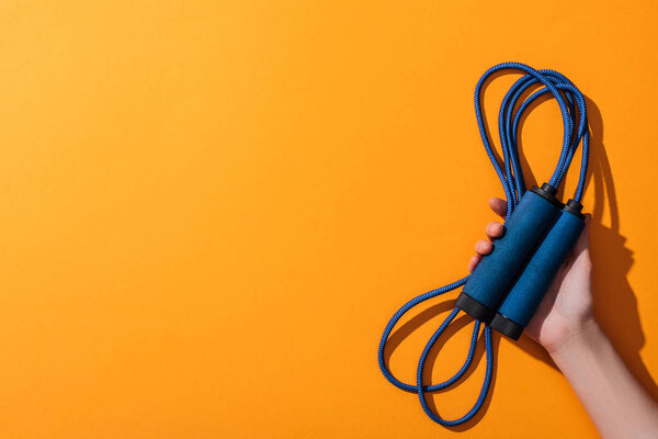 cropped view of woman holding blue jumping rope on yellow 
