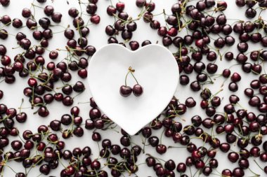 top view of red and ripe cherries on heart shaped plate  clipart