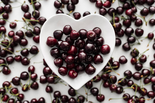 top view of ripe, fresh, whole and sweet cherries on white plate 