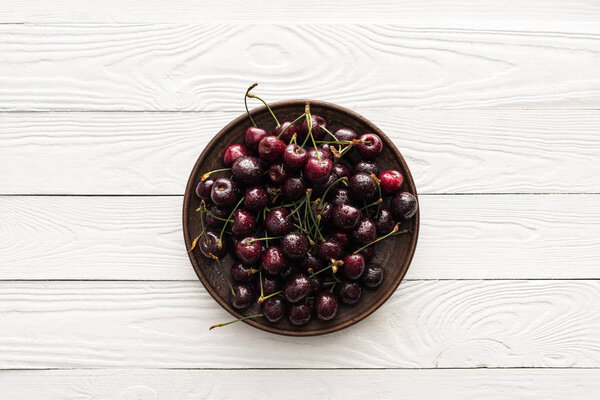 top view of fresh, sweet and wet cherries on plate on wooden background 