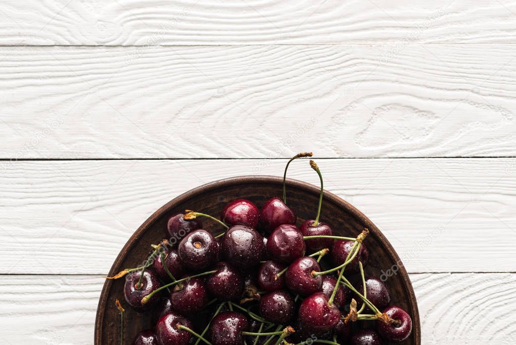 top view of fresh, sweet and washed cherries on plate on wooden background 