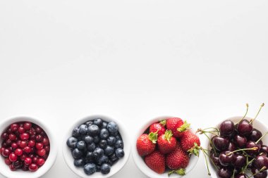 top view of sweet cranberries and blueberries, strawberries and cherries on bowls  clipart
