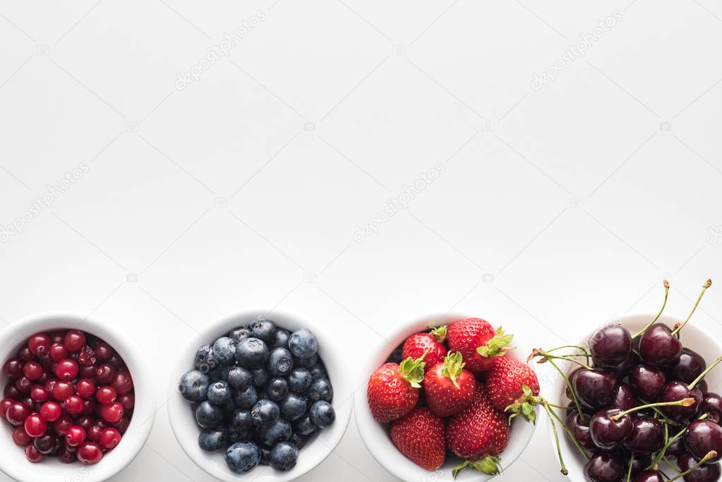 top view of sweet cranberries and blueberries, strawberries and cherries on bowls 