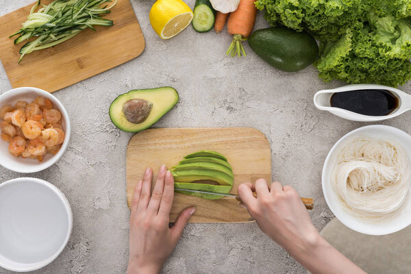 top view of woman cutting avocado with knife on cutting board 