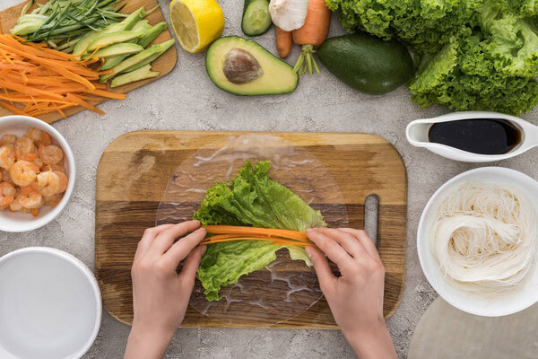 top view of woman putting cut carrot on lettuce, on cutting board 