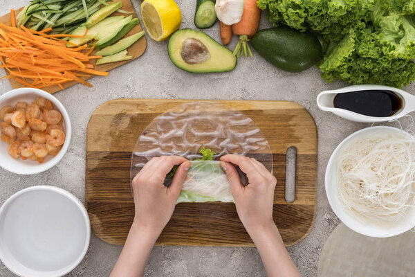 top view of woman making roll on cutting board among ingredients 